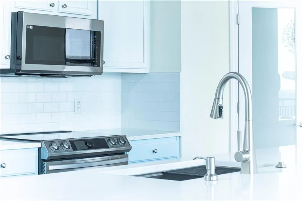 Kitchen featuring stainless steel appliances, decorative backsplash, white cabinets, and light stone counters