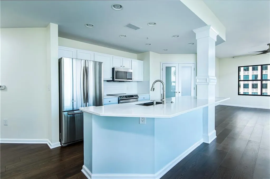 Kitchen with stainless steel appliances, dark wood-style floors, white cabinetry, a ceiling fan, and a kitchen island with sink