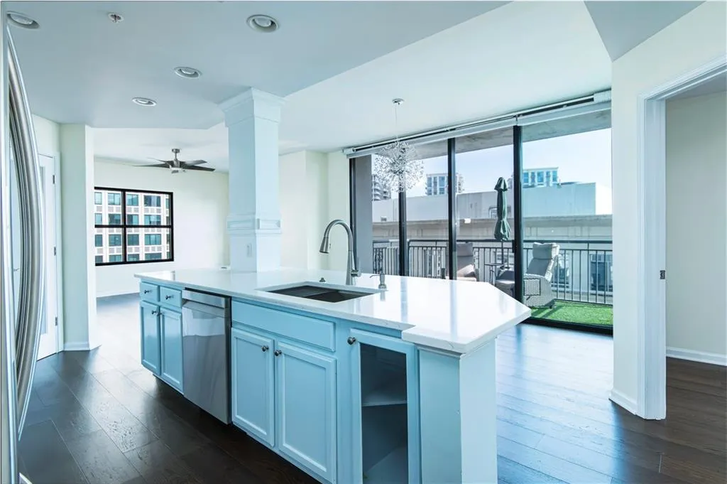 Kitchen with dark wood-type flooring, a center island with sink, decorative columns, open floor plan, and stainless steel dishwasher