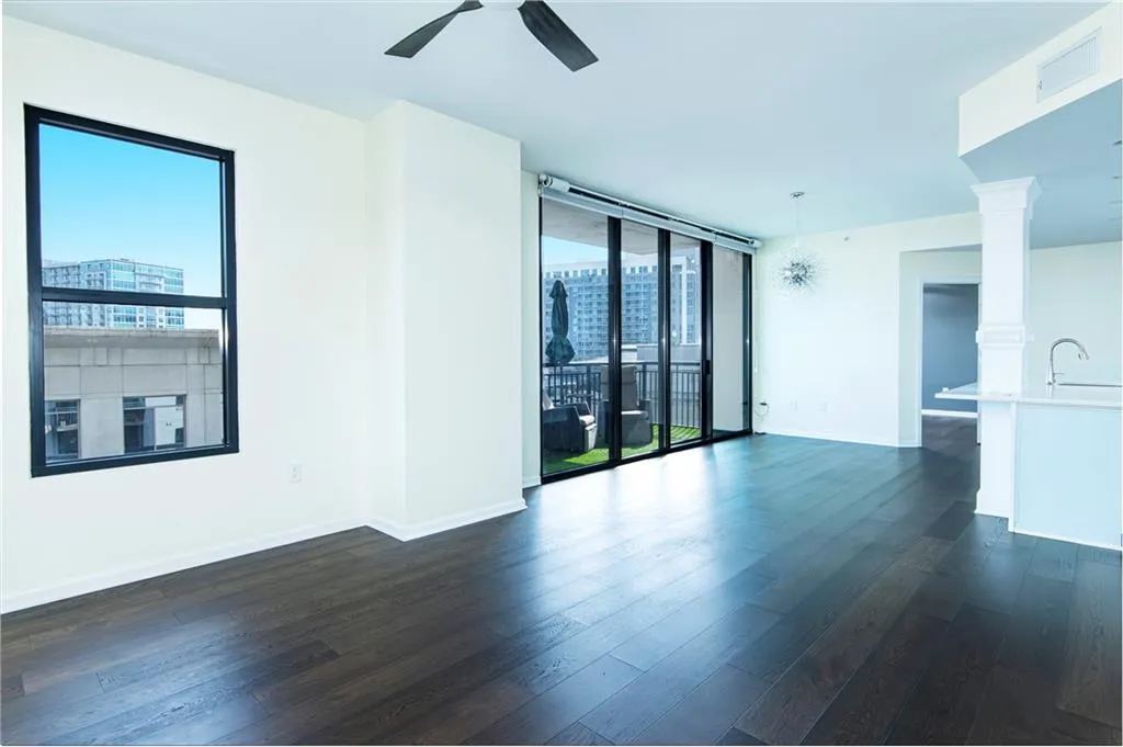 Empty room with floor to ceiling windows, dark wood-style floors, ceiling fan, and a city view