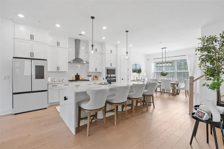 Open-concept kitchen featuring an oversized island, white shaker cabinetry, stainless steel appliances, and wood-finish flooring