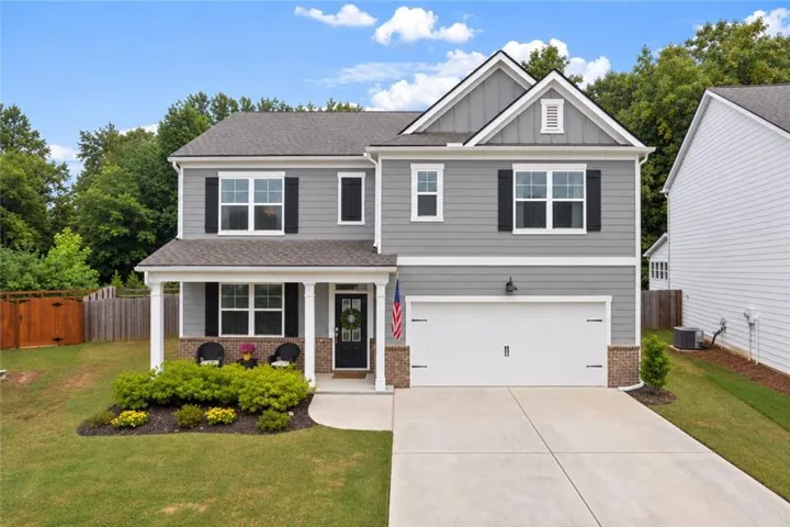 Two-story residence featuring grey siding, white trim, a covered front porch with white columns, a two-car garage, and established landscaping