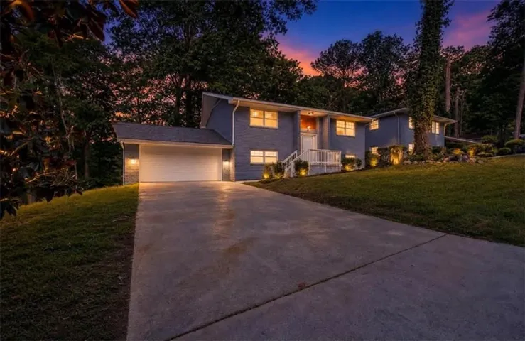 Split-level residence featuring a two-car garage, concrete driveway, and white railings leading to the entry