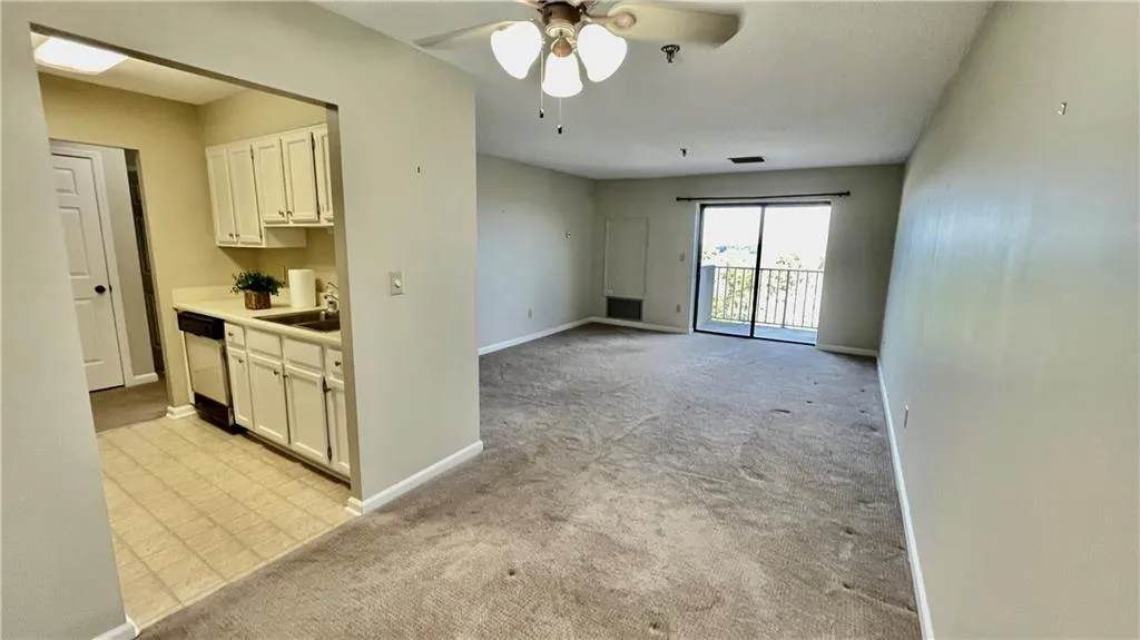 Kitchen featuring light colored carpet, ceiling fan, sink, dishwasher, and white cabinetry