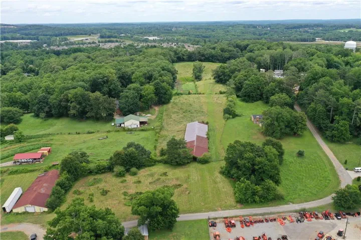 Extensive agricultural property featuring multiple structures, including a primary residence with a light green roof, a large red-roofed barn, and several outbuildings