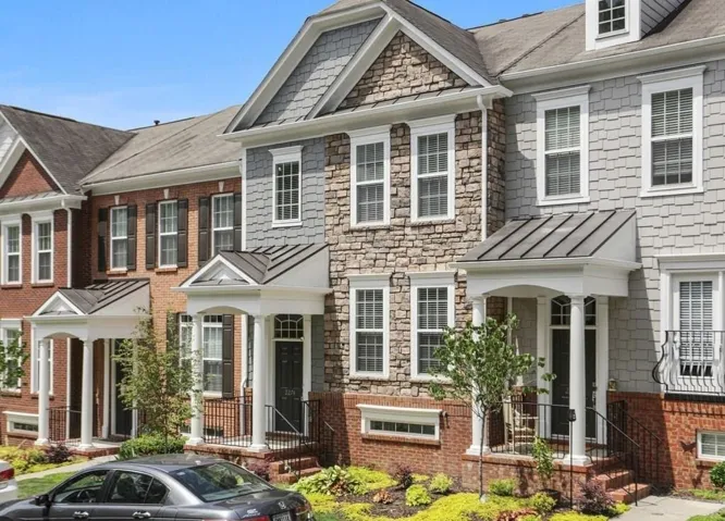 Elegant townhome featuring a mixed-material exterior with brick and stone detailing, complemented by white trim and multiple gabled rooflines