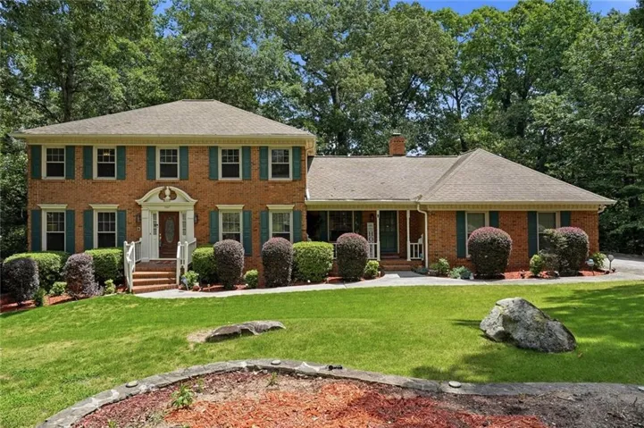Brick exterior with green shutters, a portico entry, and mature landscaping