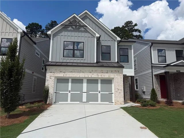 Two-story exterior with light brick and gray siding, featuring a two-car garage with a translucent door, a prominent front gable, and a metal awning over the garage