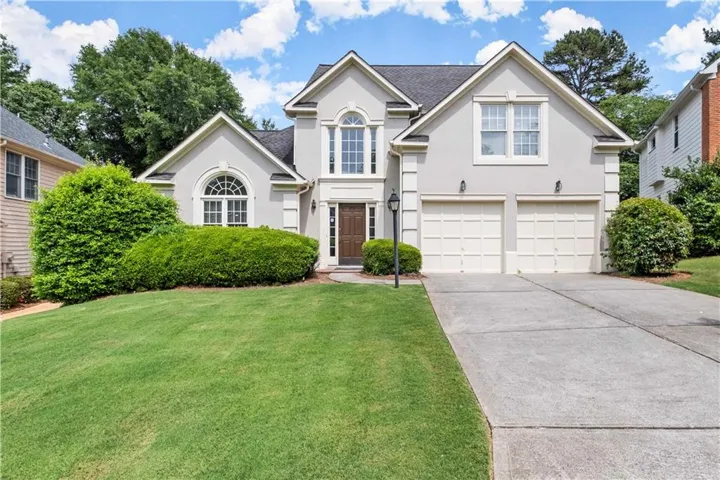 Stucco exterior with a two-car garage, arched window, and mature landscaping