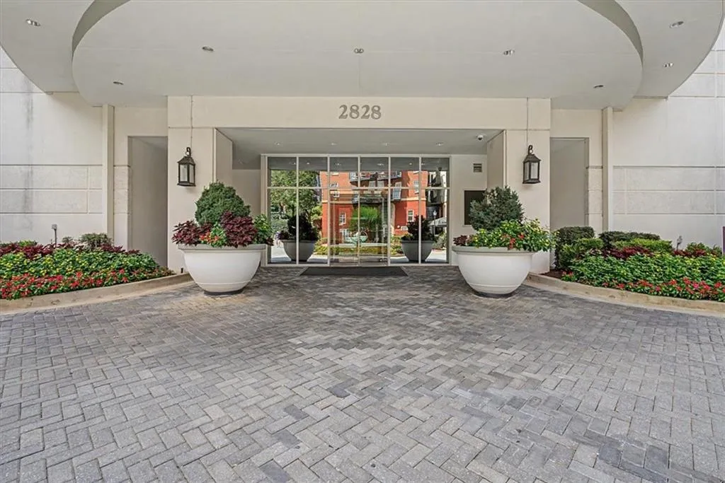 Entryway featuring a curved awning, glass double doors, sconce lighting, and decorative planters