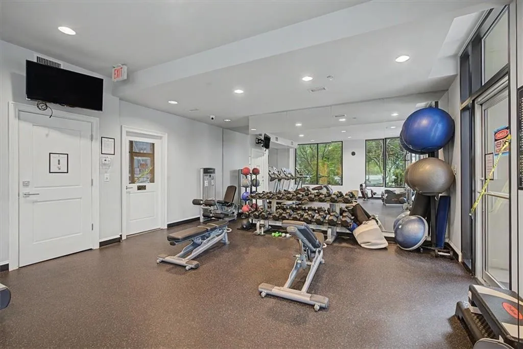 Fitness center featuring rubber flooring, recessed lighting, expansive windows, a full-wall mirror, and a wall-mounted television