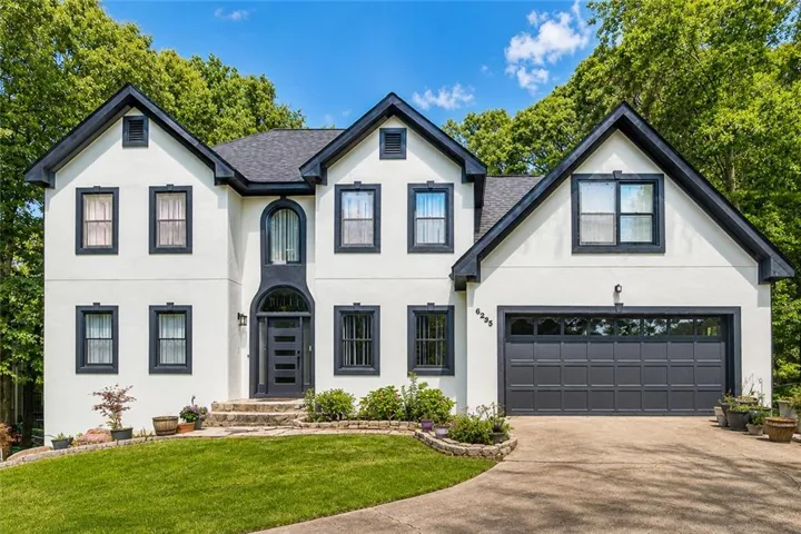 Two-story stucco exterior featuring a two-car garage with transom windows, dark trim accents, and a prominent arched entryway