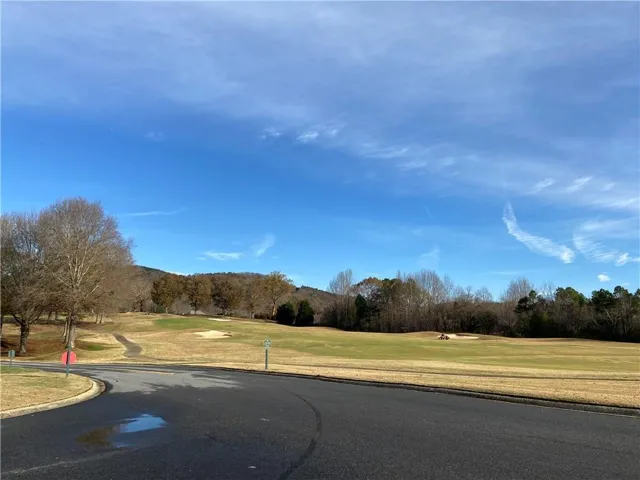 Paved street bordering a golf course with multiple greens, sand traps, and mature trees