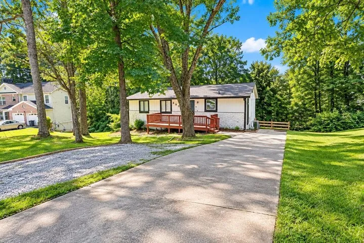 White exterior with black trim, a wood deck, a concrete driveway, and mature trees