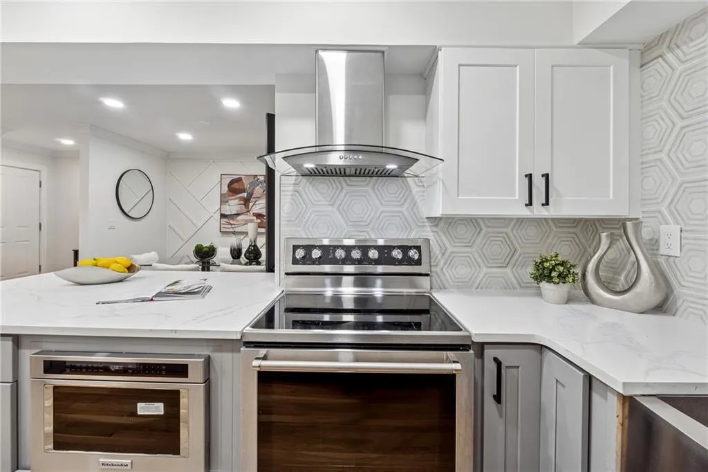 Kitchen featuring light stone counters, exhaust hood, appliances with stainless steel finishes, white cabinetry, and recessed lighting