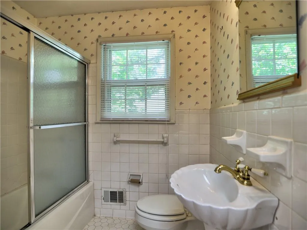 Full bathroom with a wealth of natural light, bath / shower combo with glass door, tile walls, and tile floors
