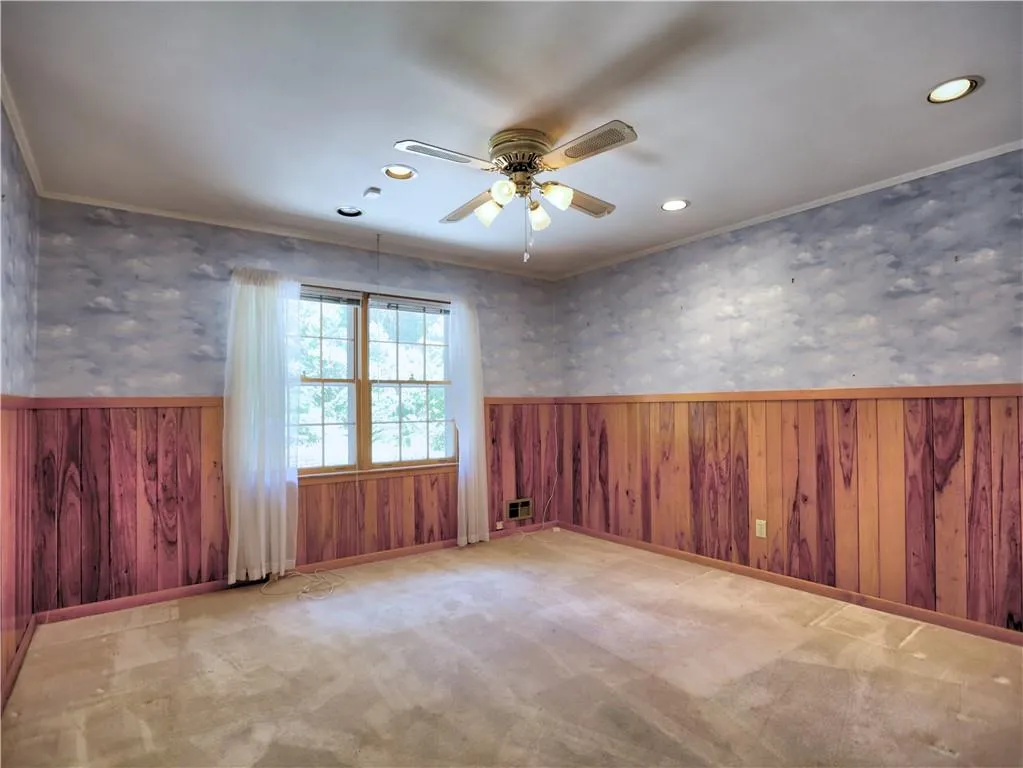 Unfurnished room featuring crown molding, wooden walls, carpet floors, and ceiling fan