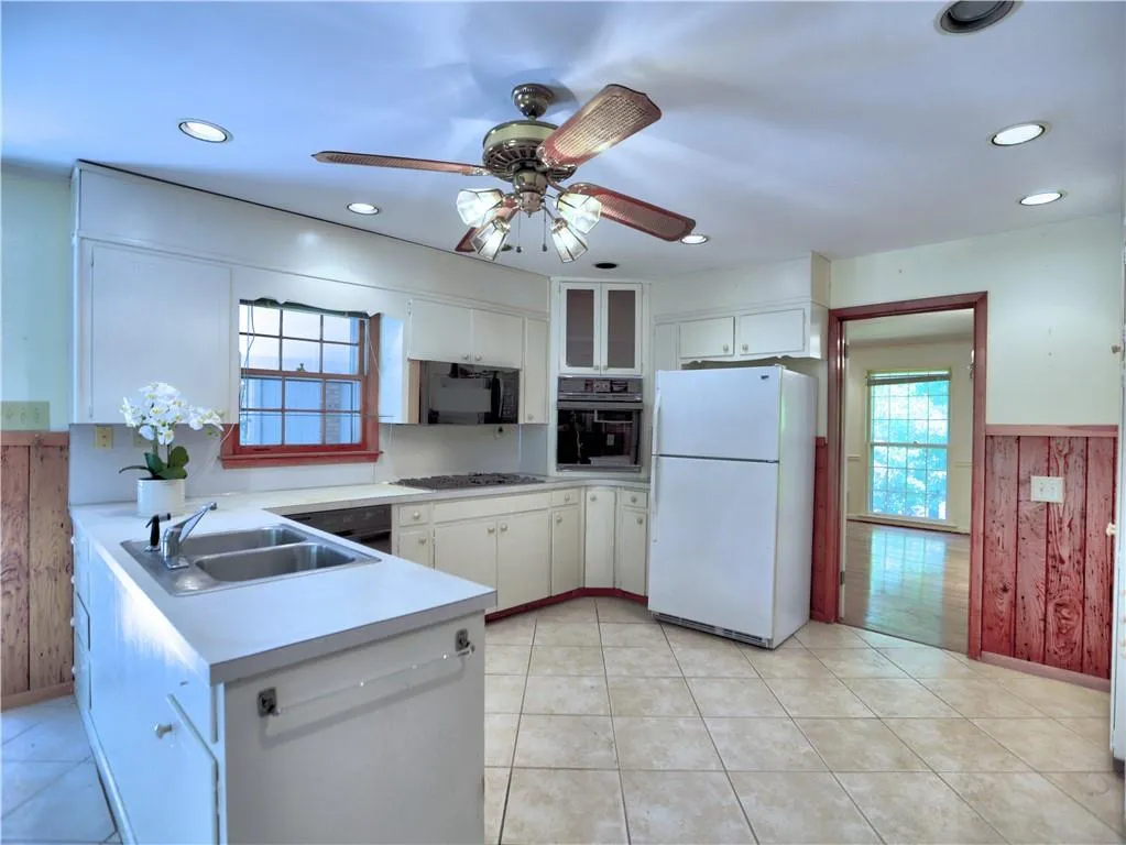 Kitchen with kitchen peninsula, ceiling fan, black appliances, white cabinets, and sink