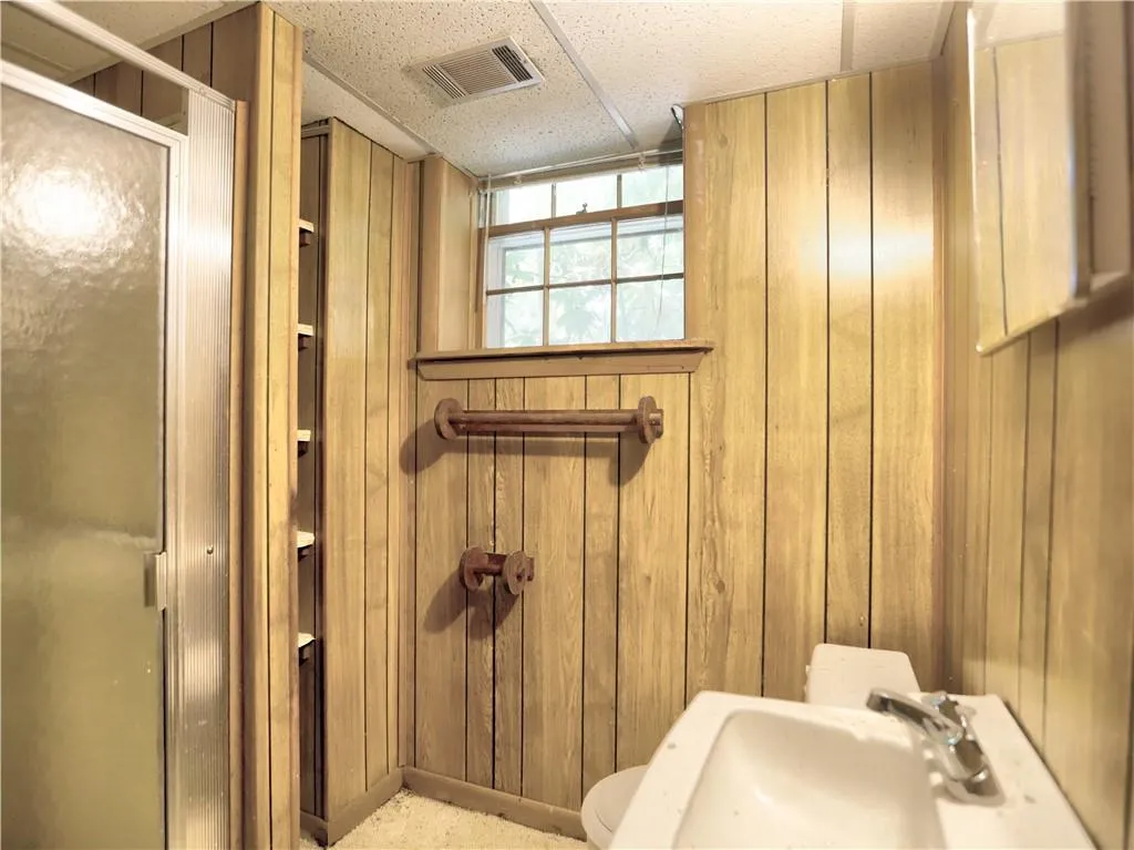Bathroom featuring walk in shower, wood walls, a drop ceiling, sink, and toilet