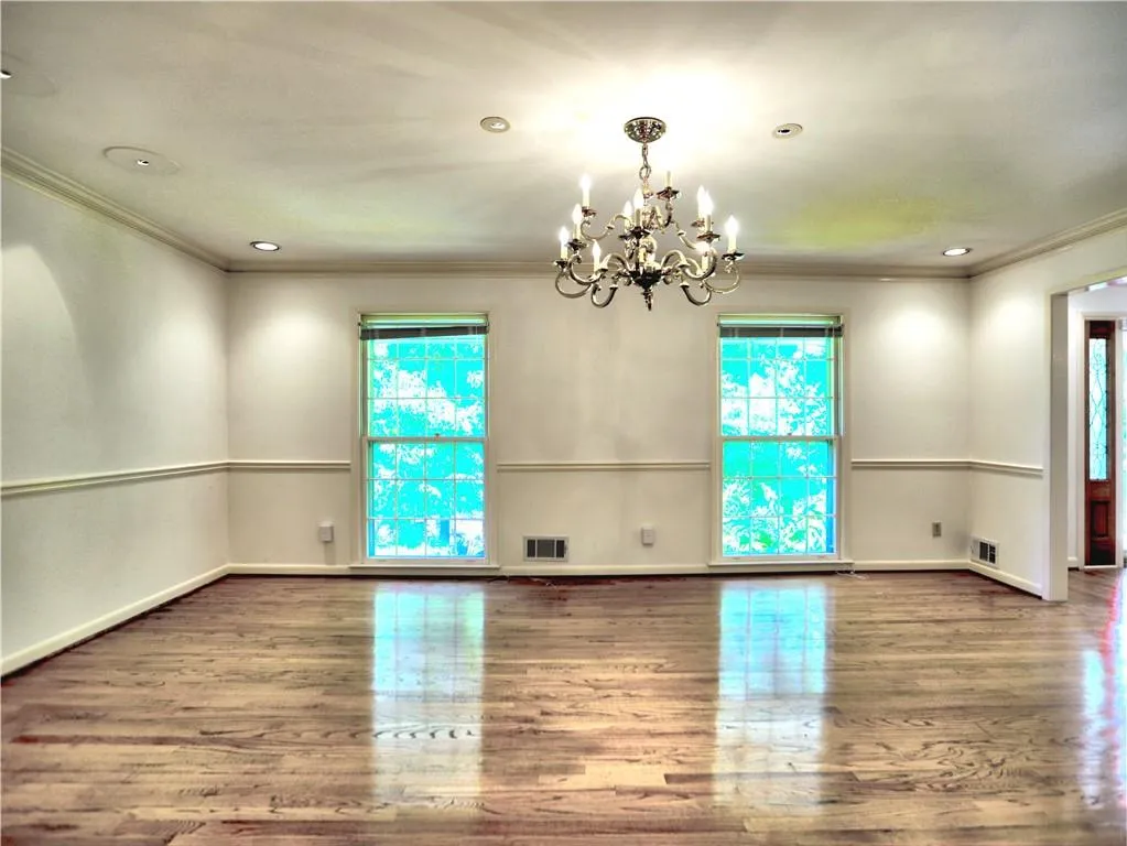 Empty room featuring ornamental molding, hardwood / wood-style flooring, a wealth of natural light, and a chandelier