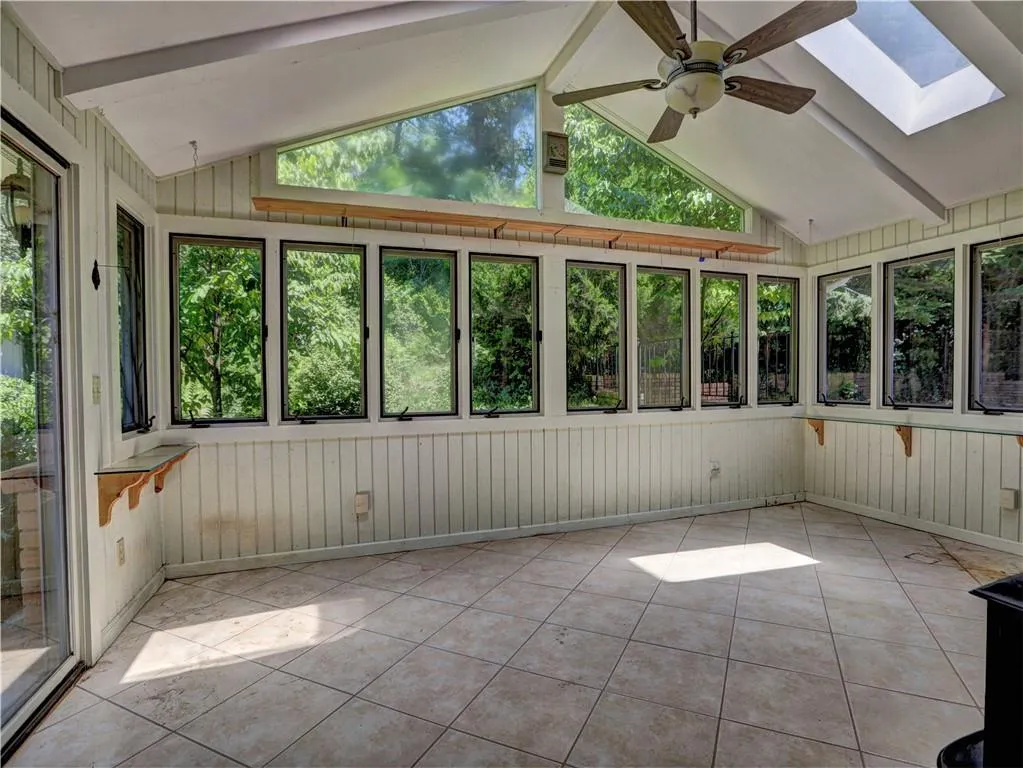 Unfurnished sunroom featuring ceiling fan and vaulted ceiling with skylight