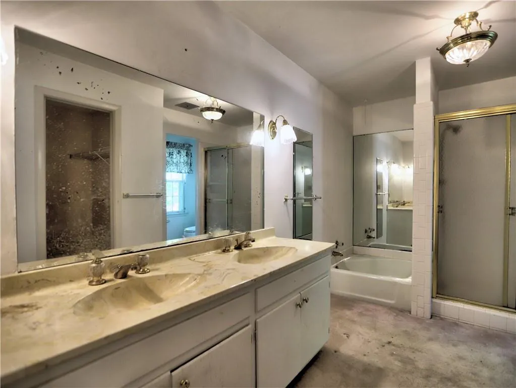 Bathroom with double sink, shower with separate bathtub, concrete flooring, and vanity with extensive cabinet space