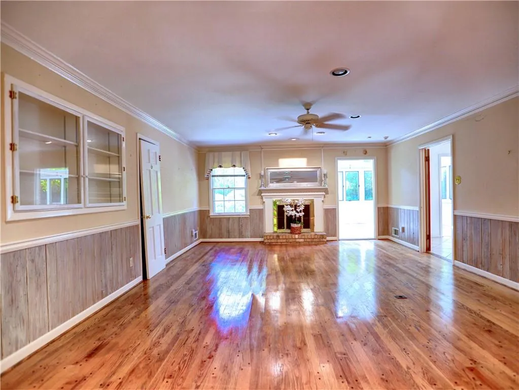 Unfurnished living room featuring wood-type flooring, ceiling fan, a fireplace, and crown molding