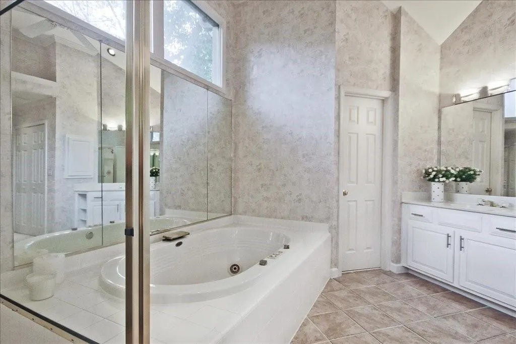 Full bathroom featuring a tub with jets, vanity, light tile patterned floors, lofted ceiling, and wallpapered walls