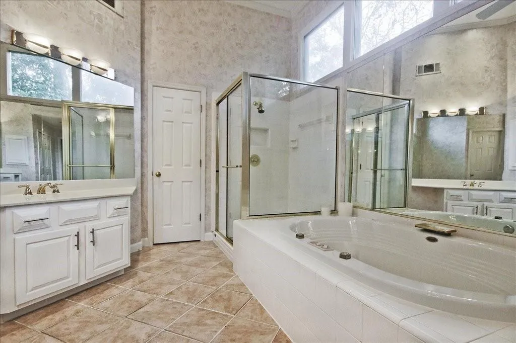 Bathroom featuring a garden tub, a shower stall, vanity, light tile patterned floors, and a towering ceiling