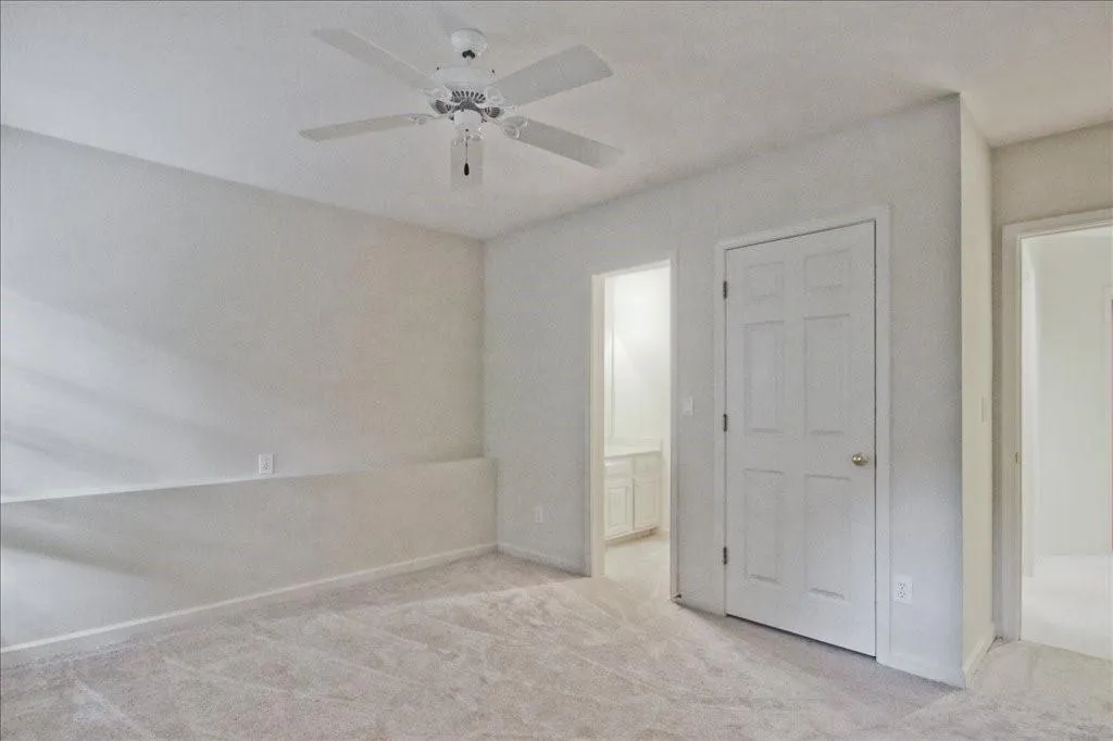 Unfurnished bedroom with light carpet, ensuite bath, and ceiling fan
