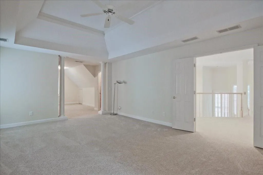 Unfurnished room with light colored carpet, ceiling fan, and a tray ceiling