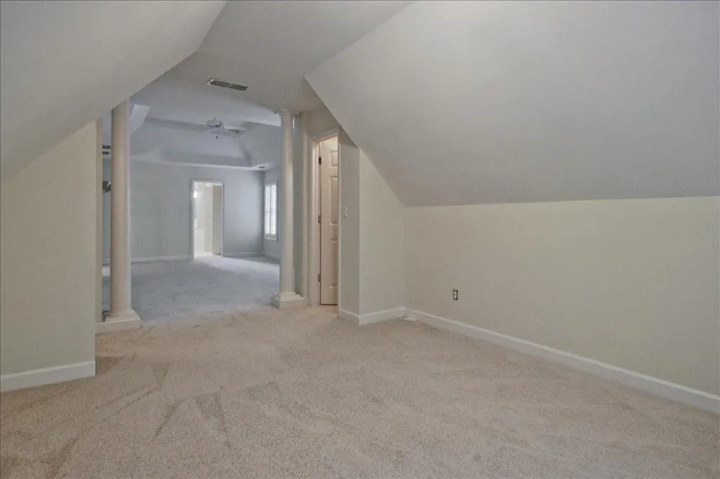 Bonus room with light carpet, vaulted ceiling, decorative columns, and ceiling fan