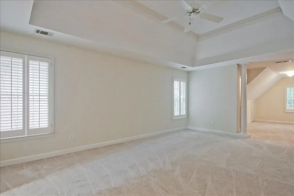 Empty room with light carpet, a tray ceiling, a ceiling fan, and ornate columns