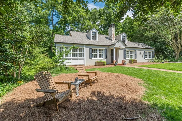 Traditional-style residence featuring dormer windows, a prominent brick chimney, and dark louvered shutters
