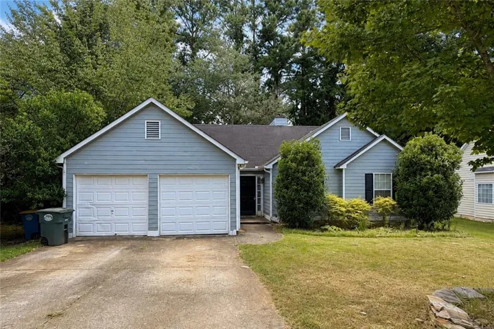 Light blue siding exterior with a dark roof, featuring a two-car garage, a concrete driveway, and front landscaping
