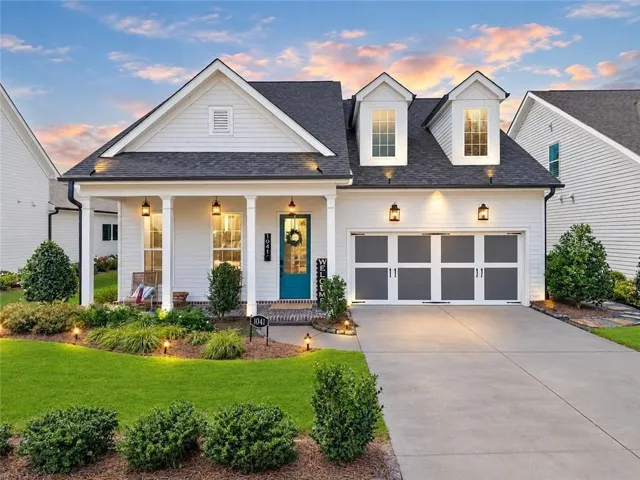 White-sided exterior with a dark shingle roof, featuring a covered front porch with white columns and a vibrant teal front door