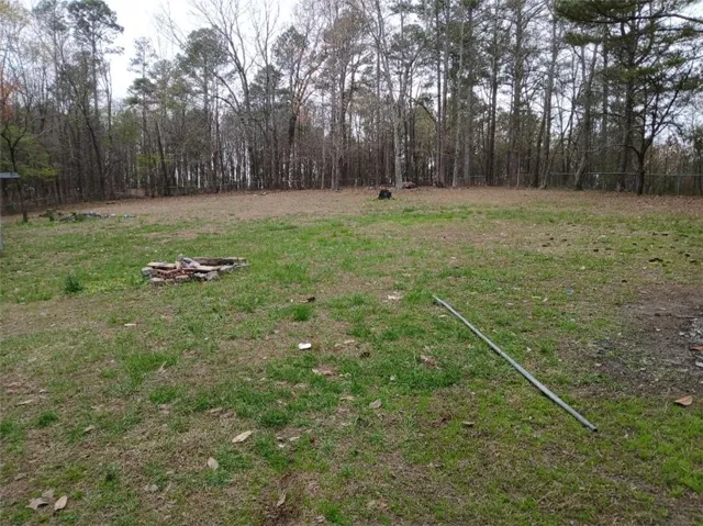 Expansive grassy area featuring a partial brick perimeter structure and a backdrop of mature trees