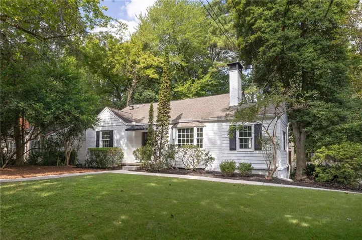 White clapboard exterior with dark shutters, gabled roofline, and prominent brick chimney