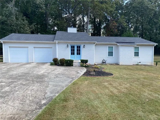 Ranch-style home featuring a garage, a front lawn, a shingled roof, driveway, and a chimney
