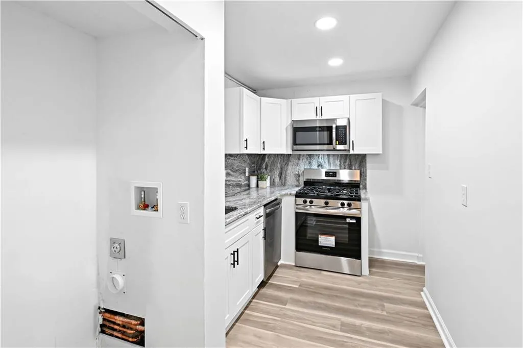 Kitchen with light stone countertops, appliances with stainless steel finishes, white cabinets, tasteful backsplash, and light wood finished floors