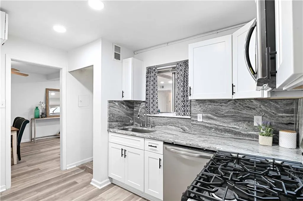 Kitchen featuring appliances with stainless steel finishes, light stone counters, white cabinetry, tasteful backsplash, and light wood finished floors