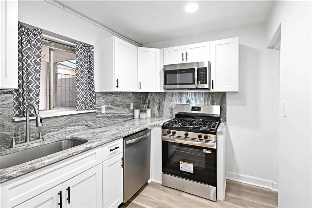 Kitchen with stainless steel appliances, white cabinets, light stone countertops, and decorative backsplash