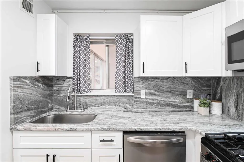 Kitchen featuring tasteful backsplash, light stone counters, stainless steel appliances, and white cabinets