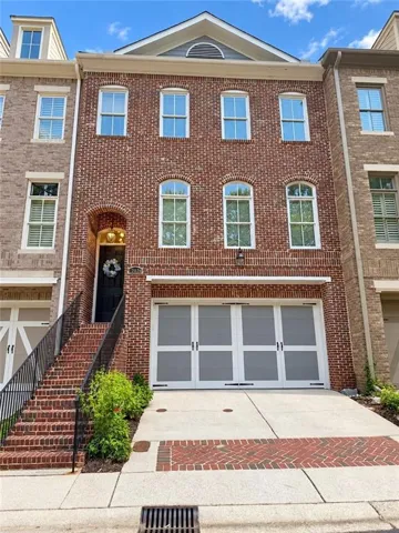 Three-story brick exterior with arched windows, a two-car garage, and a brick-paved driveway