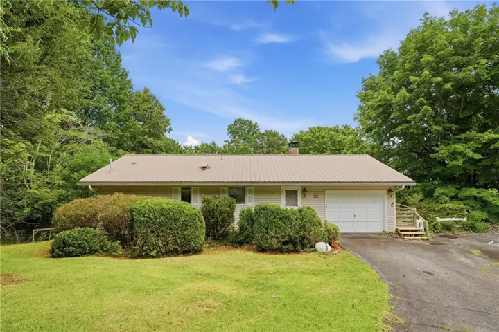 Ranch-style residence featuring a metal roof, attached garage, and a paved driveway
