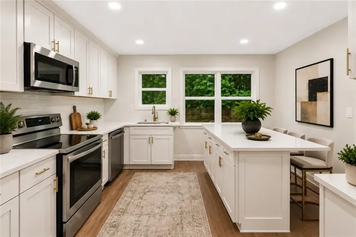 Bright, updated kitchen featuring white cabinetry with brushed nickel hardware, stainless steel appliances, white subway tile backsplash, and quartz countertops