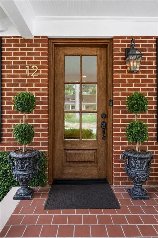 Brick facade with a wood-finish entry door featuring glass window panes, complemented by a lantern-style exterior light fixture and a tiled front porch