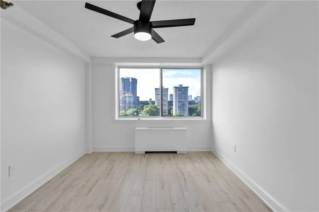 Empty room featuring radiator, a ceiling fan, light wood-type flooring, a view of skyline, and a textured ceiling