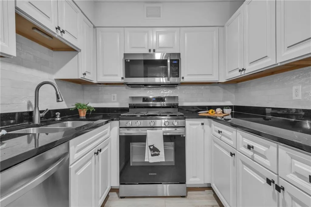 Kitchen featuring appliances with stainless steel finishes, white cabinets, backsplash, and dark stone counters