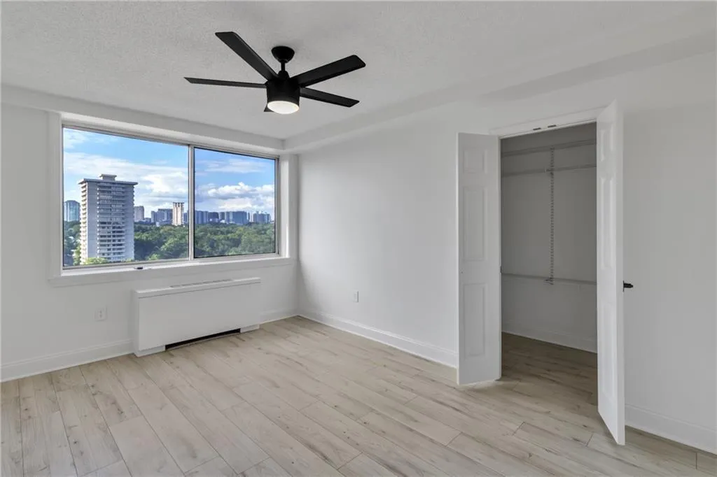 Unfurnished bedroom with radiator heating unit, light wood-type flooring, a city view, a ceiling fan, and a textured ceiling